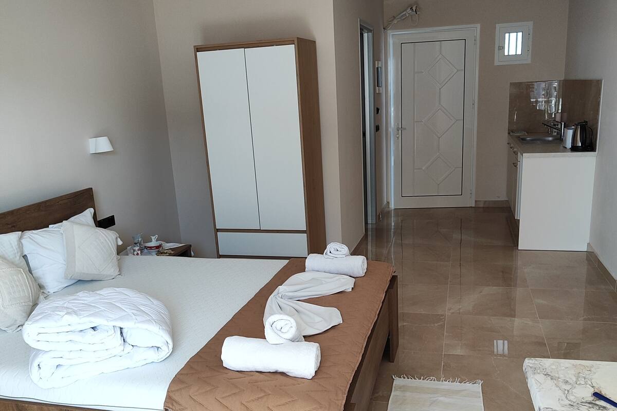 A hotel room with a bed, a wooden bench, a bathroom, and a kitchenette.