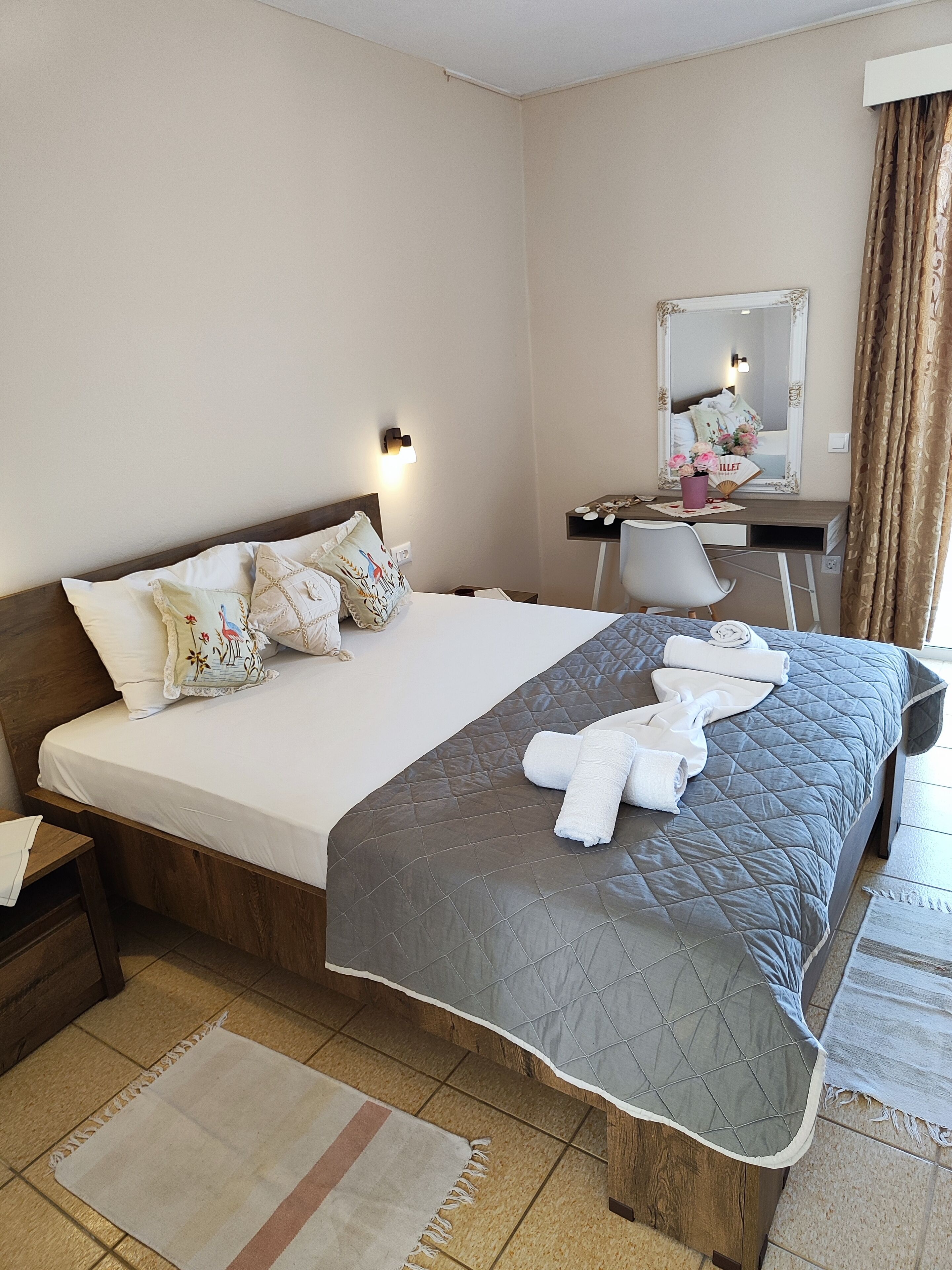 A hotel room with a bed, a desk, a chair, a mirror, and a window with curtains.