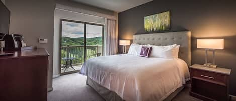 A hotel room with a large bed, two bedside tables, a coffee maker, and a view of a balcony.