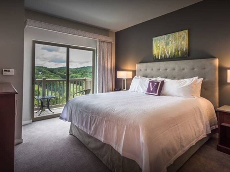 A hotel room with a large bed, two bedside tables, a coffee maker, and a view of a balcony.