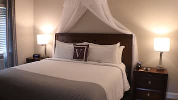 Una habitación de hotel con cama a dosel, dos lámparas de noche, una mesita de noche con un reloj y una mesita junto a la cama con una lámpara.