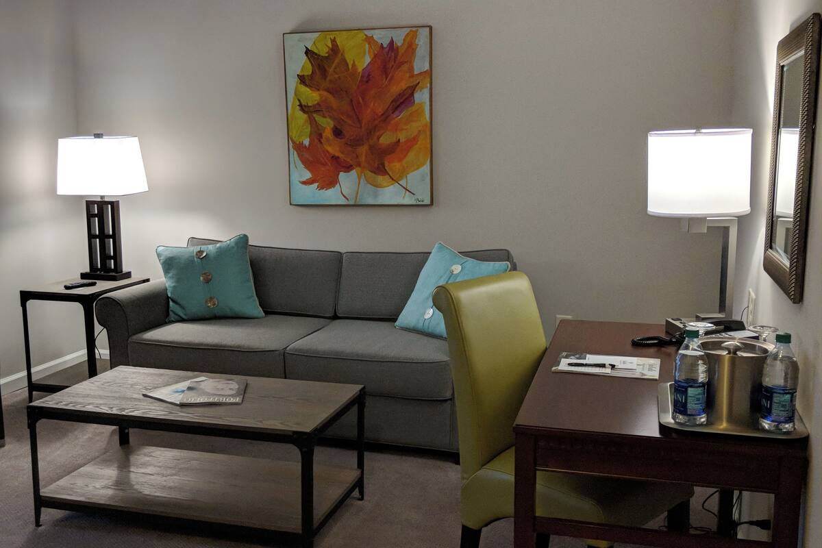 A living room with a sofa, a coffee table, a desk, two lamps, and a painting on the wall.