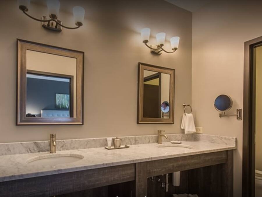 A hotel bathroom with two sinks, a large mirror, and wall-mounted lighting.