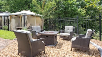An outdoor patio with wicker furniture, a stone fire table, and a covered seating area.