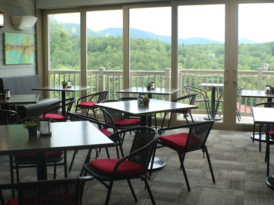A restaurant with multiple tables and chairs, large windows with a view of a forested mountain range.