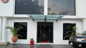 Entrada de hotel con una puerta negra, un felpudo rojo y dos macetas.