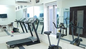 Un gimnasio con cintas de correr, bicicletas estáticas y un espejo grande.