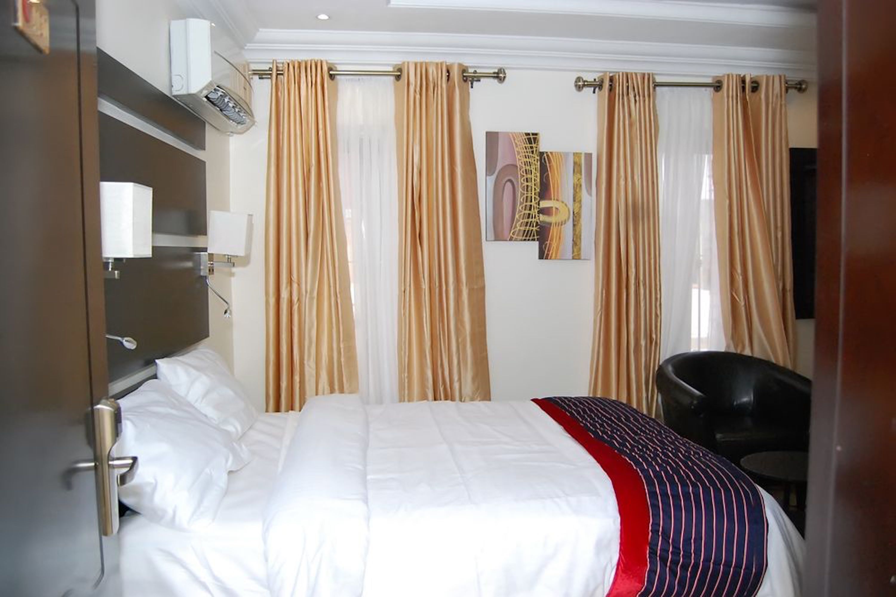 A hotel room with a bed, a chair, a wall-mounted air conditioner, and curtains.