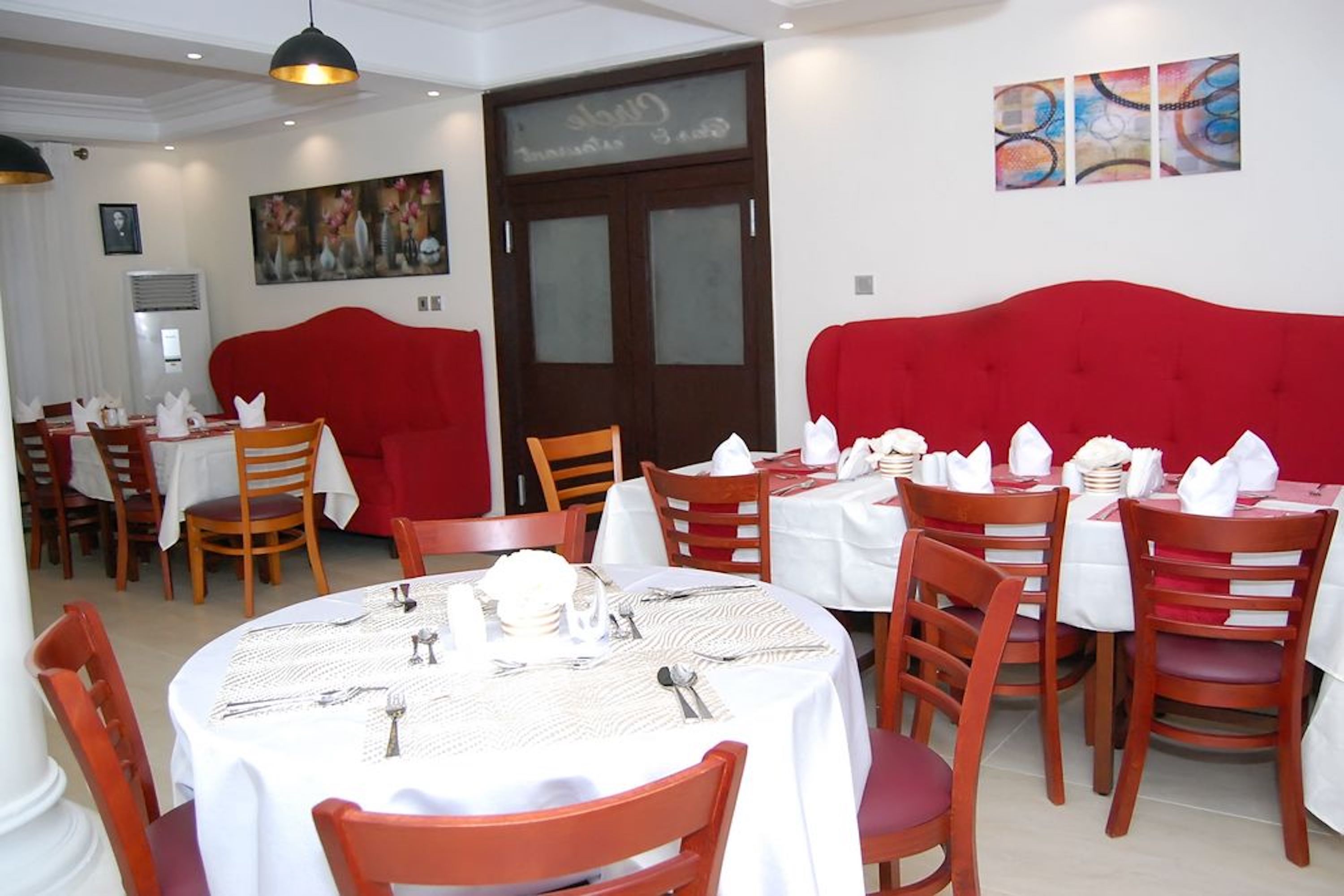 Un espace repas avec des tables rondes, des chaises à revêtement rouge et des nappes blanches.