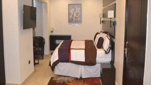 Habitación de hotel con cama, mesita de noche, lámpara y televisor de pantalla plana montado en la pared.
