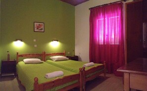 Una habitación con dos camas individuales, paredes verdes, un cabecero de madera, una mesita de noche con lámpara y una ventana con cortinas rojas.