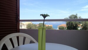 A balcony with a white chair and a table, a green vase with a plant, and a view of buildings and water. - Ionian Breeze Apartments (Corfu)