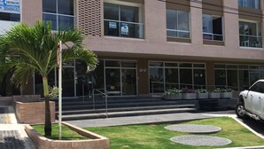 A modern building with a brick facade, large windows, and a well-maintained lawn with circular planters. - Apartamento Ejecutivo Ancora (Barranquilla)