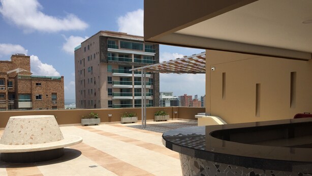 A rooftop terrace with a stone table, potted plants, and a view of a hotel building. - Apartamento Ejecutivo Ancora (Barranquilla)