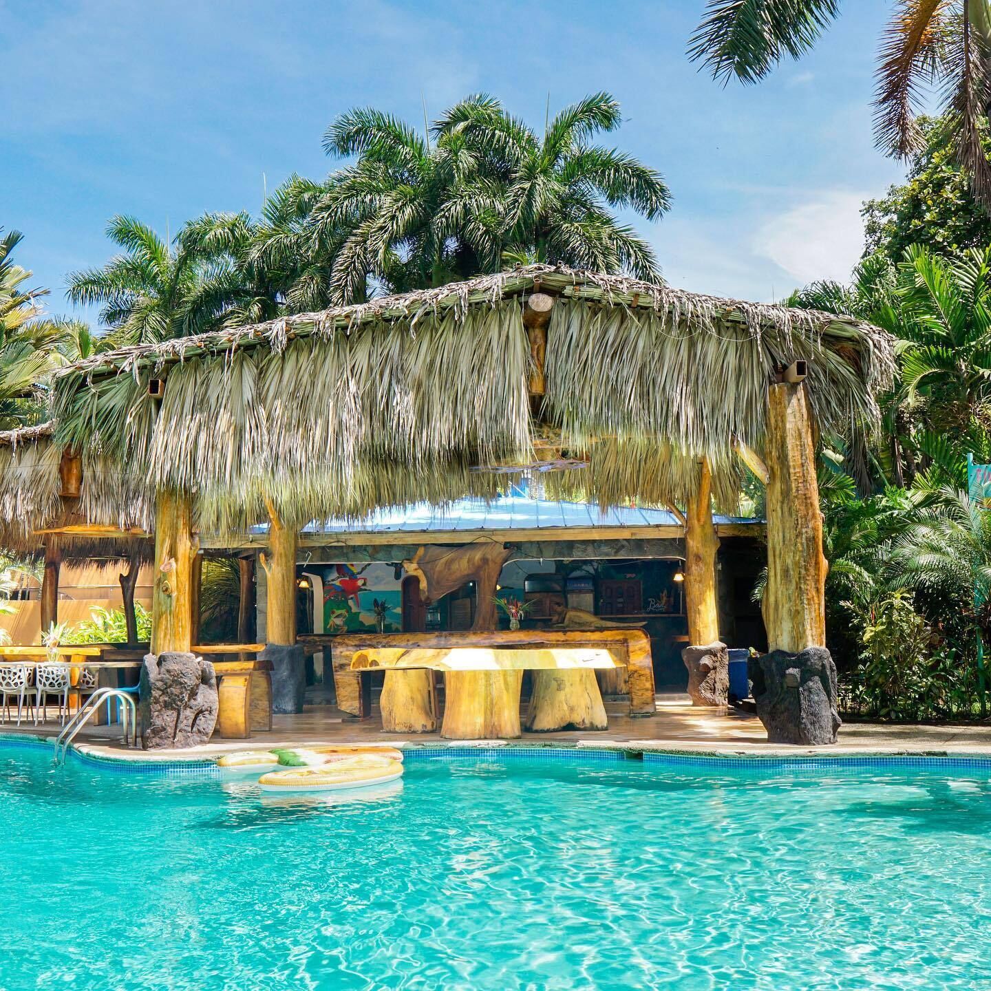 A pool area with a thatched roof structure, wooden seating, and a bar area.