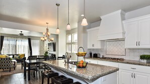 A spacious kitchen with a large island, white cabinetry, and pendant lighting. - Poolside Perfection (St. George)