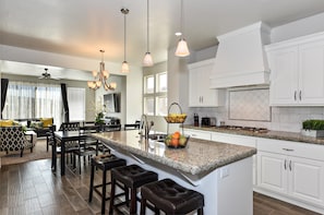 A spacious kitchen with a large island, white cabinetry, and pendant lighting.