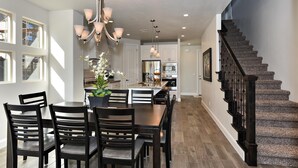 A modern kitchen with white cabinets, a central island, and a staircase with a dark railing. - Poolside Perfection (St. George)
