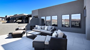 An outdoor patio with wicker furniture, large windows, and a view of the desert. - Poolside Perfection (St. George)