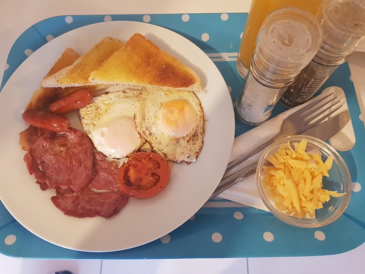 Une assiette de petit-déjeuner comprenant des toasts, des œufs, du bacon, des tomates et du fromage.
