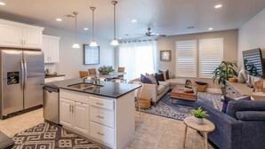 Una cocina moderna con una isla central, muebles blancos, electrodomésticos de acero inoxidable, iluminación colgante y un ventilador de techo.