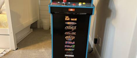 Un couloir étroit où se trouve une borne d’arcade bleue, sur laquelle figurent différents titres de jeux.