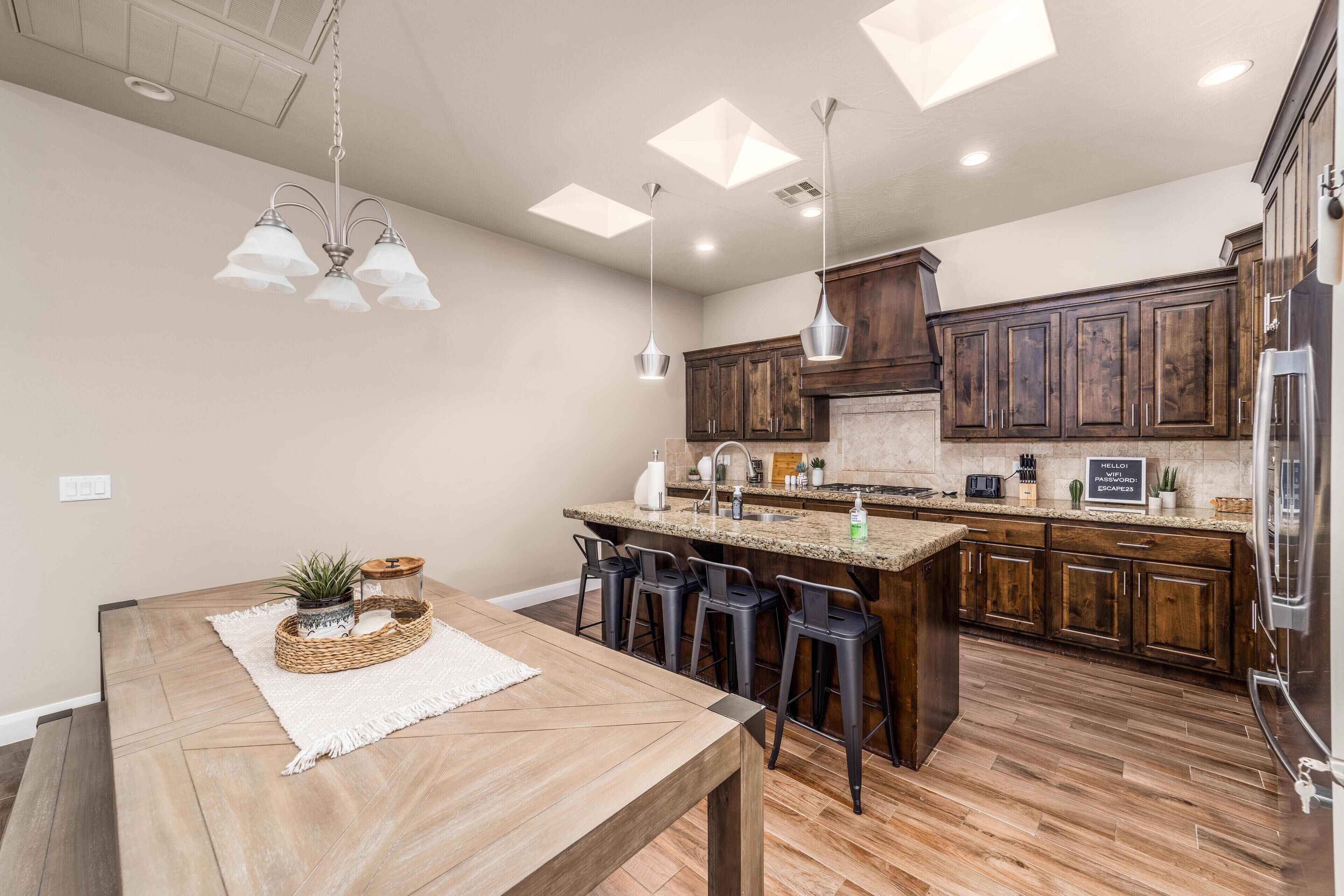 A modern kitchen with wooden cabinets, a central island with bar stools, pendant lighting, and a backsplash.