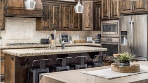 A modern kitchen with dark wooden cabinets, a granite countertop, stainless steel appliances, and bar stools. - Snow Canyon Hideaway (St. George)
