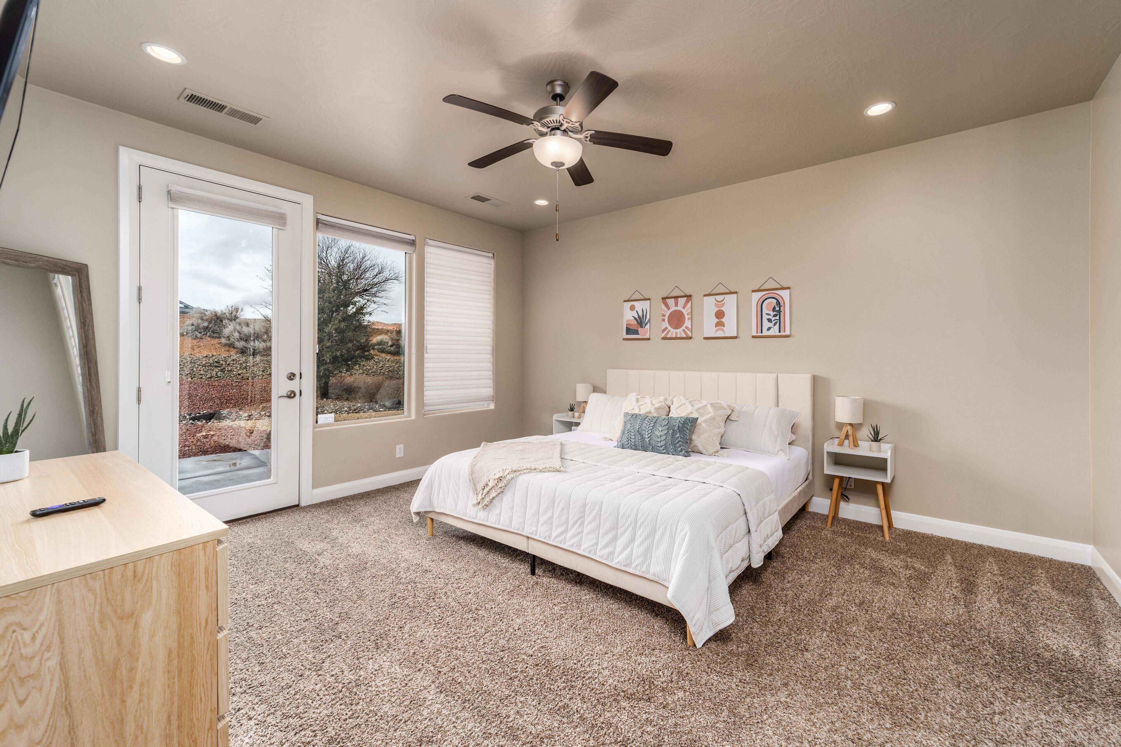 A bedroom with a bed, a ceiling fan, a nightstand, and a desk.