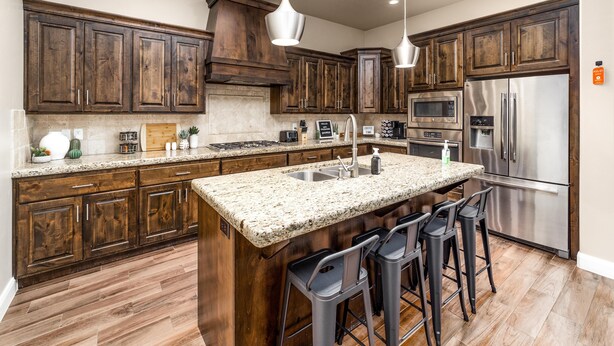 A modern kitchen with dark wooden cabinets, granite countertops, stainless steel appliances, and bar stools. - Snow Canyon Hideaway (St. George)