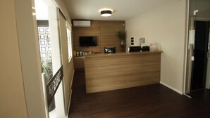 A reception area with a wooden reception desk, a flat-screen TV, a potted plant, and a wall-mounted air conditioner. - Kennedy Slim Hotel (Sao Jose)