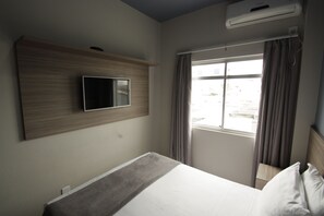 Habitación de hotel con cama, televisor montado, aire acondicionado y ventana con cortinas.