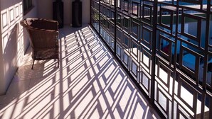 A sunlit corridor with a view through a metal grid, a wicker chair, and two potted plants. - Kennedy Slim Hotel (Sao Jose)