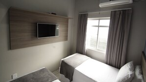 A hotel room with a flat-screen TV mounted on a wooden panel, a window with curtains, and an air conditioning unit. - Kennedy Slim Hotel (Sao Jose)