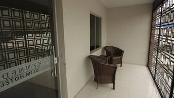 Quarto de hotel com porta de vidro, duas cadeiras de vime, uma janela e chão de azulejos.