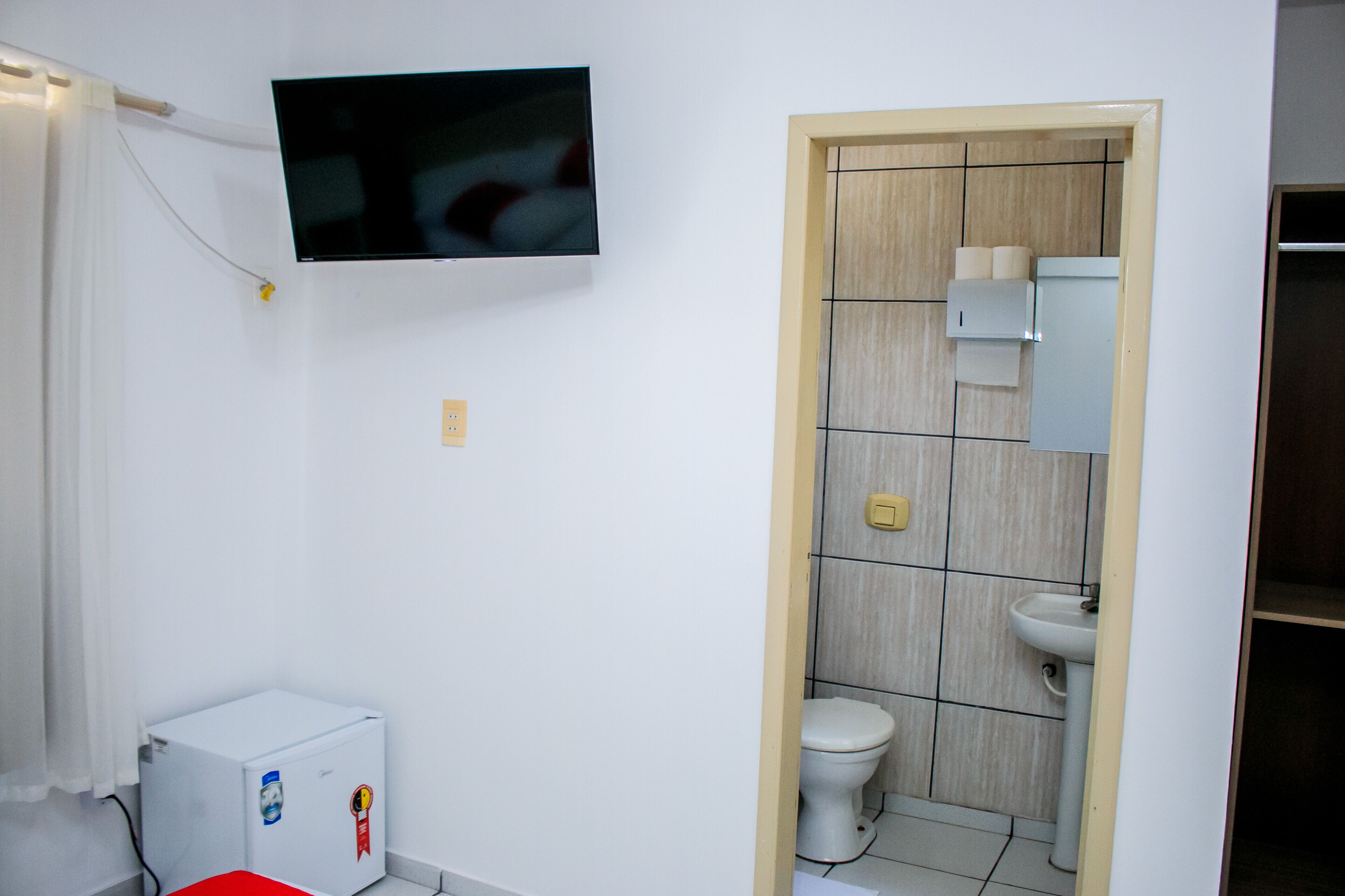 A small, compact bathroom with a toilet, sink, and a television mounted on the wall.