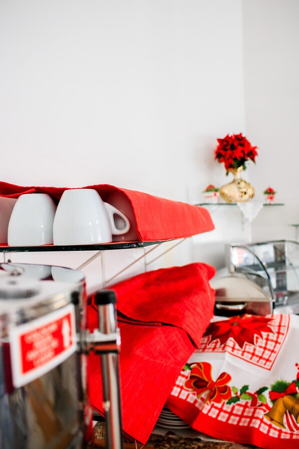 Una zona de cocina con una cafetera, un paño rojo y una taza blanca sobre una estantería.