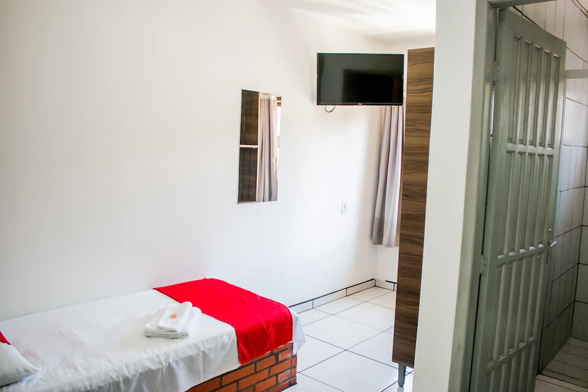 A hotel room with a single bed, a TV mounted on the wall, and a door leading to a hallway.