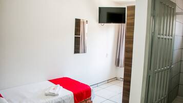 Una habitació d'hotel amb un llit individual, un televisor fixat a la paret i una porta que dona a un passadís.