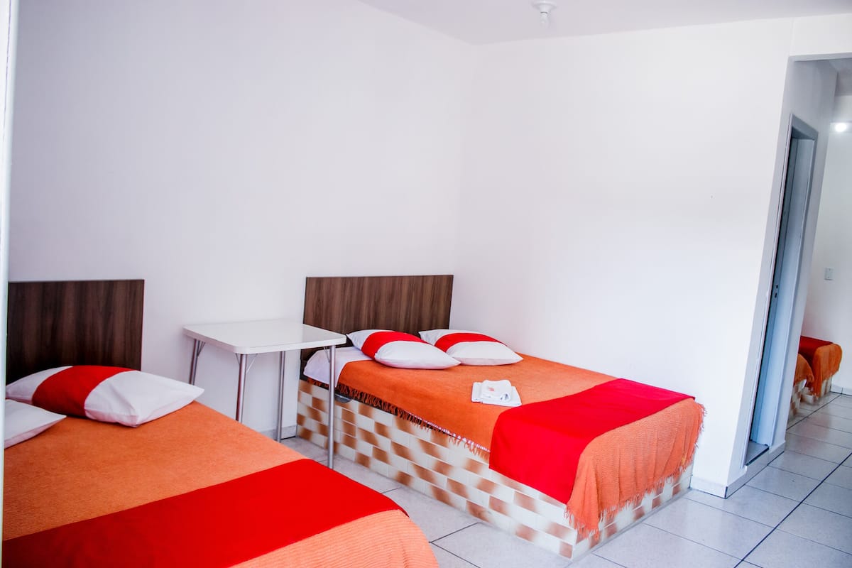 A hotel room with two beds, a small table, and a mirror.
