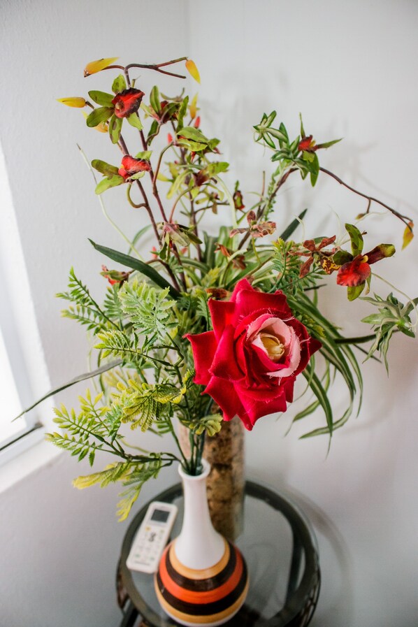 A vase with a red rose and green foliage on a table. - Hotel Palugi (Joinville)