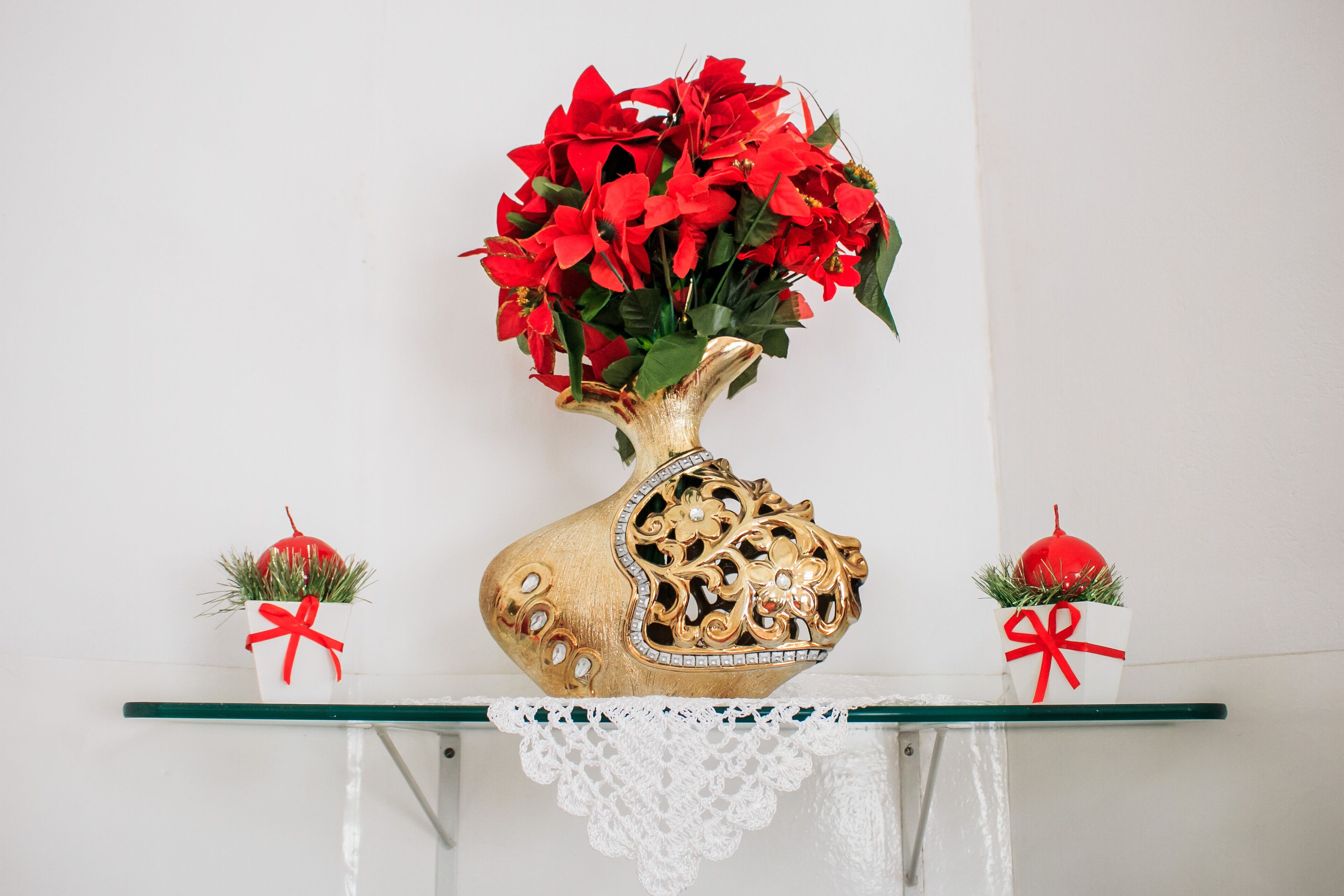 Un jarrón decorativo con flores rojas sobre un estante de vidrio.