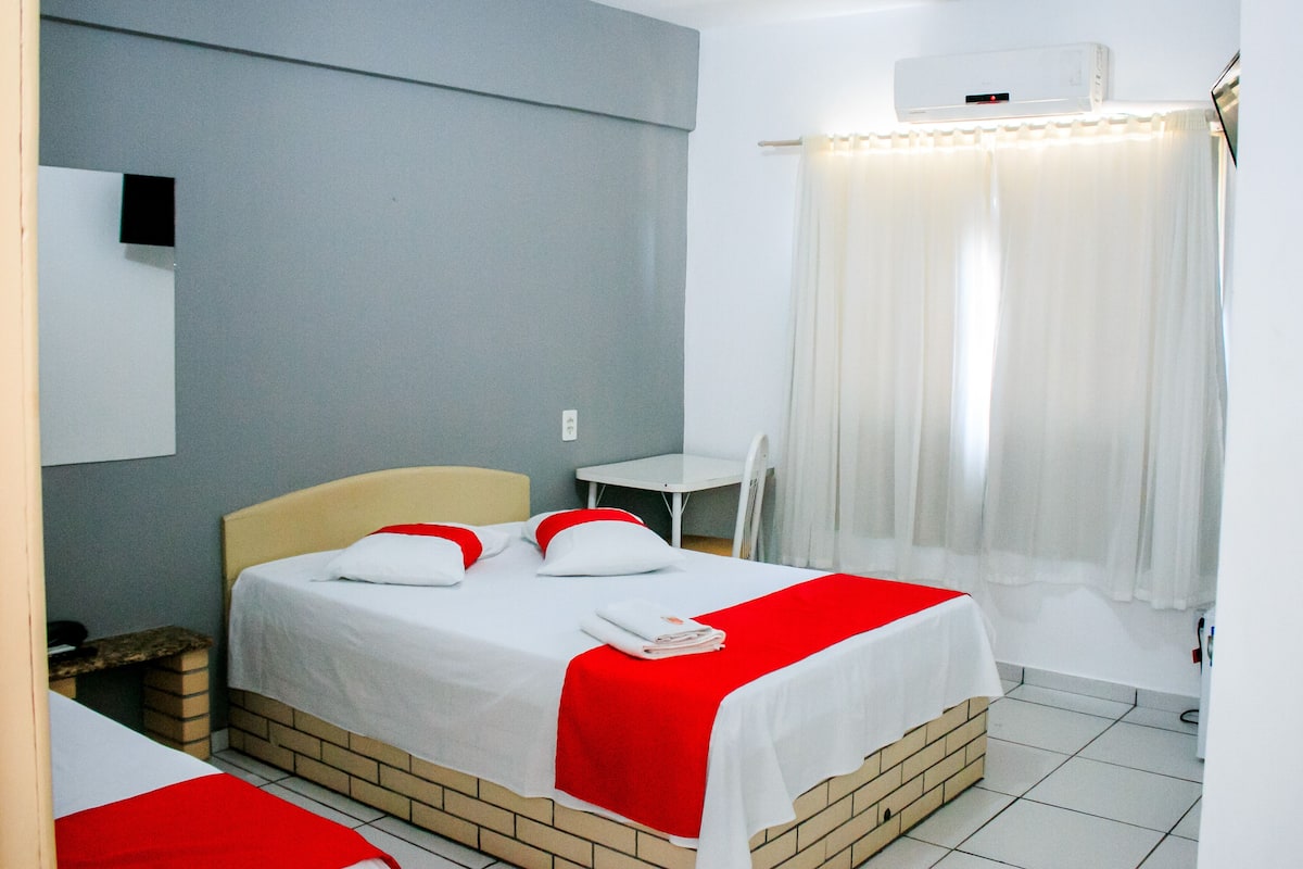 A hotel room with a bed, a small table, and a window with curtains.