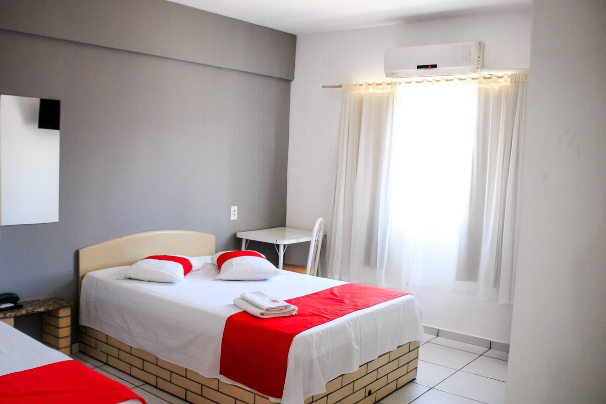 A hotel room with a bed, a desk, and a window with curtains.