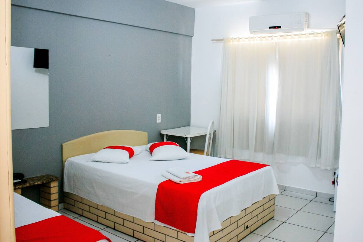 A hotel room with a single bed, a small table, a chair, and a window with curtains.