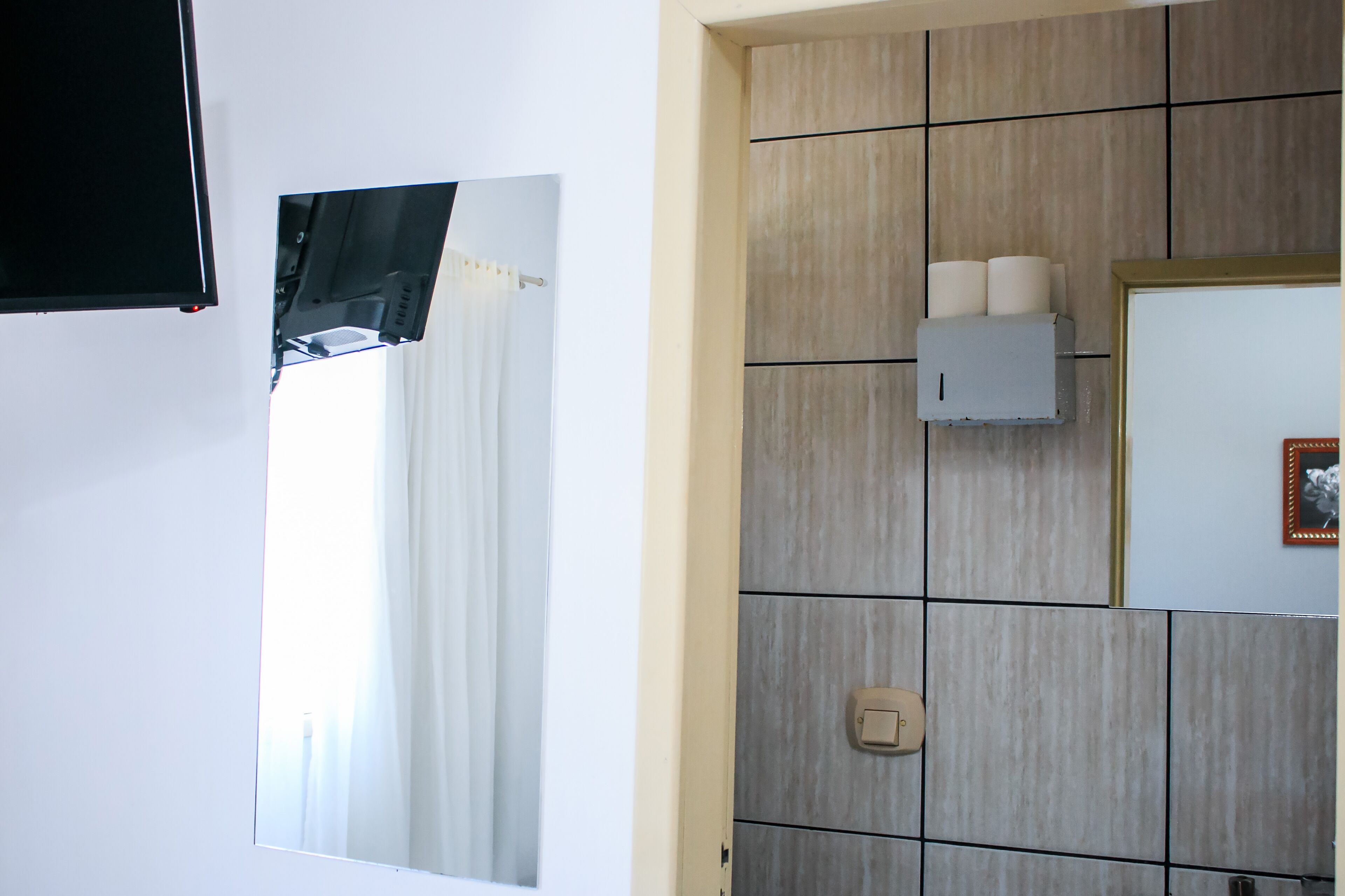 A bathroom with a mirror, a towel rack, a toilet paper holder, and a light switch.