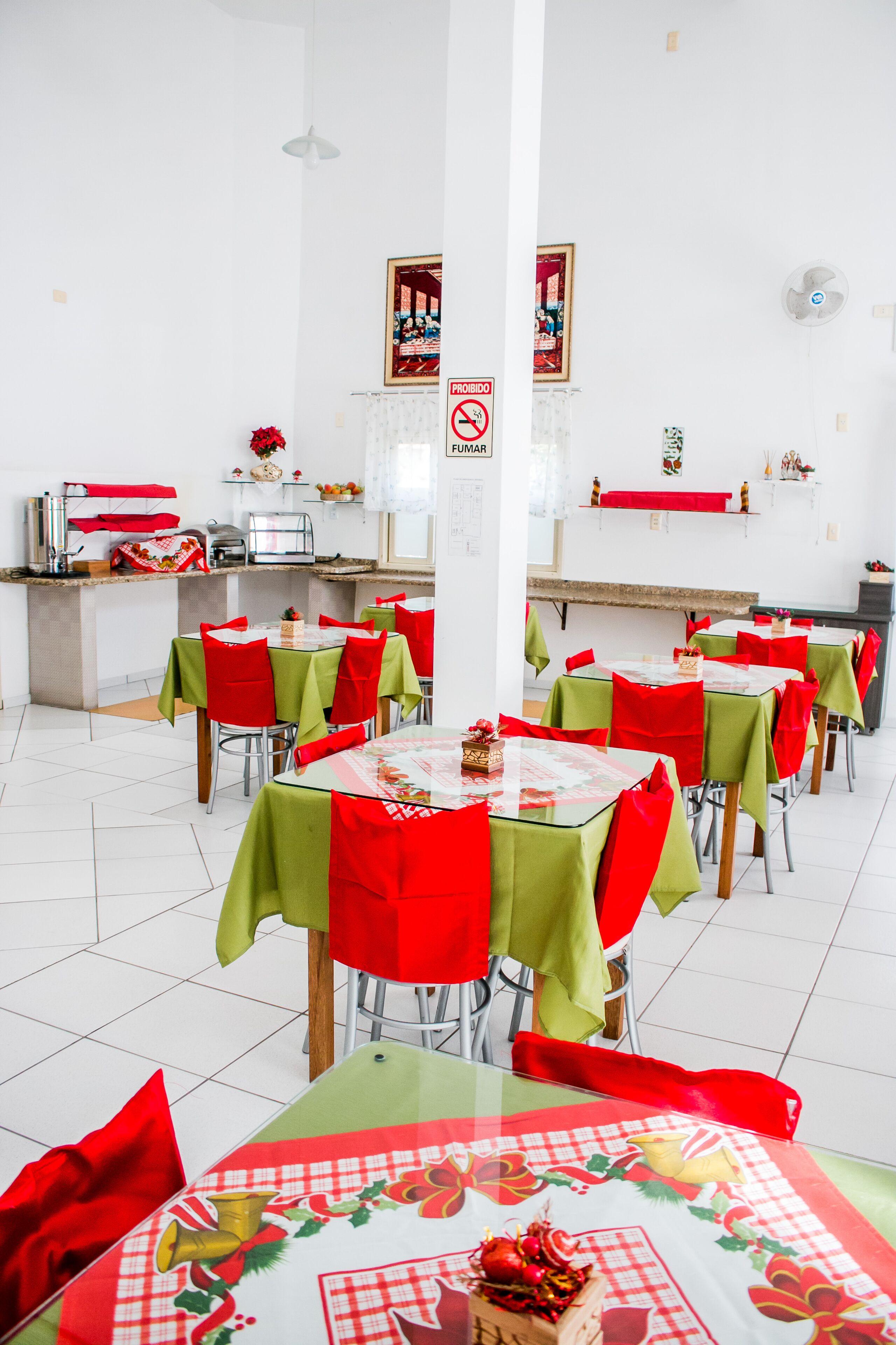 Un espace repas avec des tables disposées pour accueillir plusieurs personnes, un coin cuisine et un panneau « Il est interdit de fumer » sur le mur.