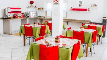 Un espace repas avec des tables disposées pour accueillir plusieurs personnes, un coin cuisine et un panneau « Il est interdit de fumer » sur le mur.