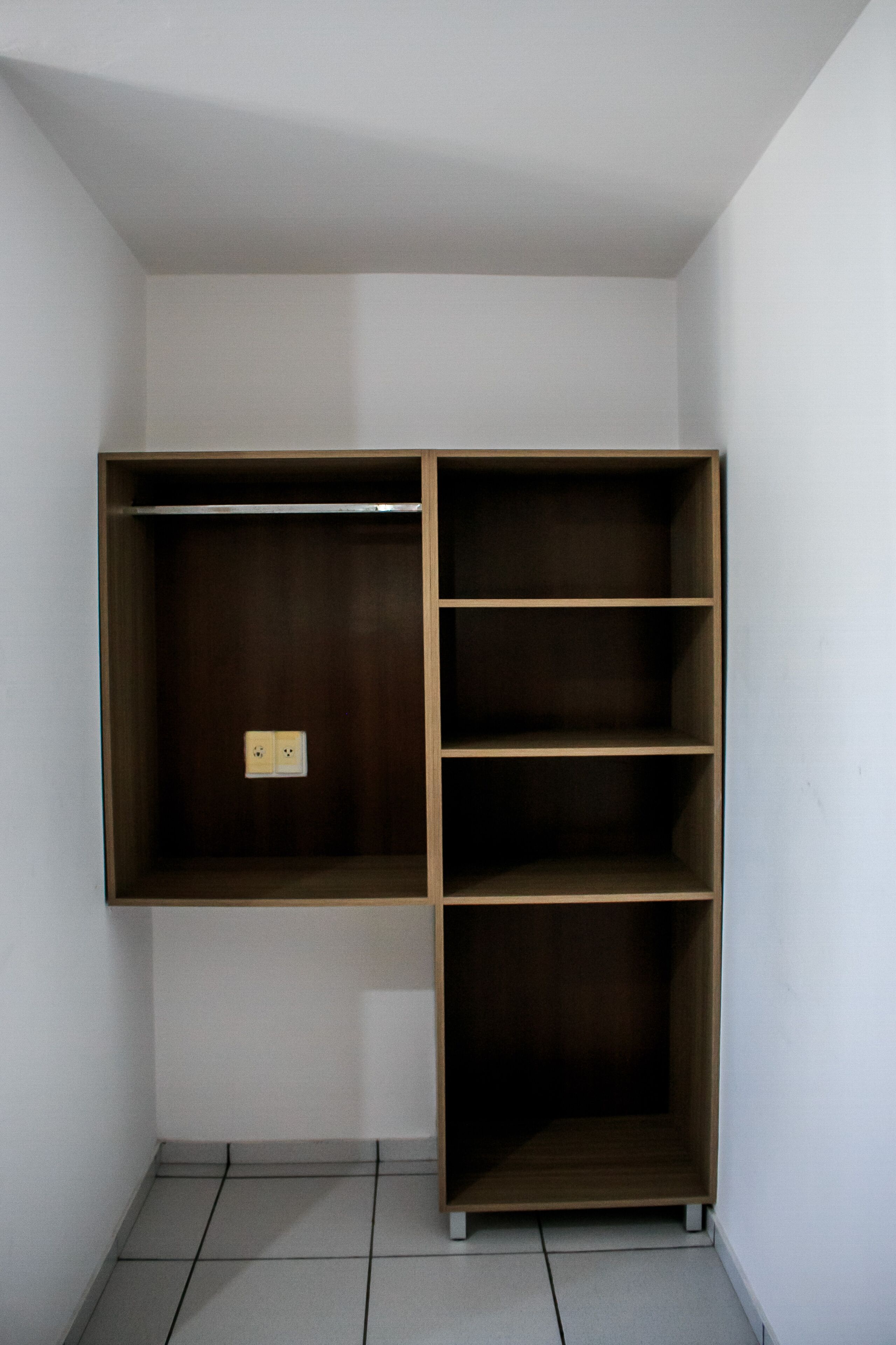 A corner closet with wooden shelving and a power outlet.