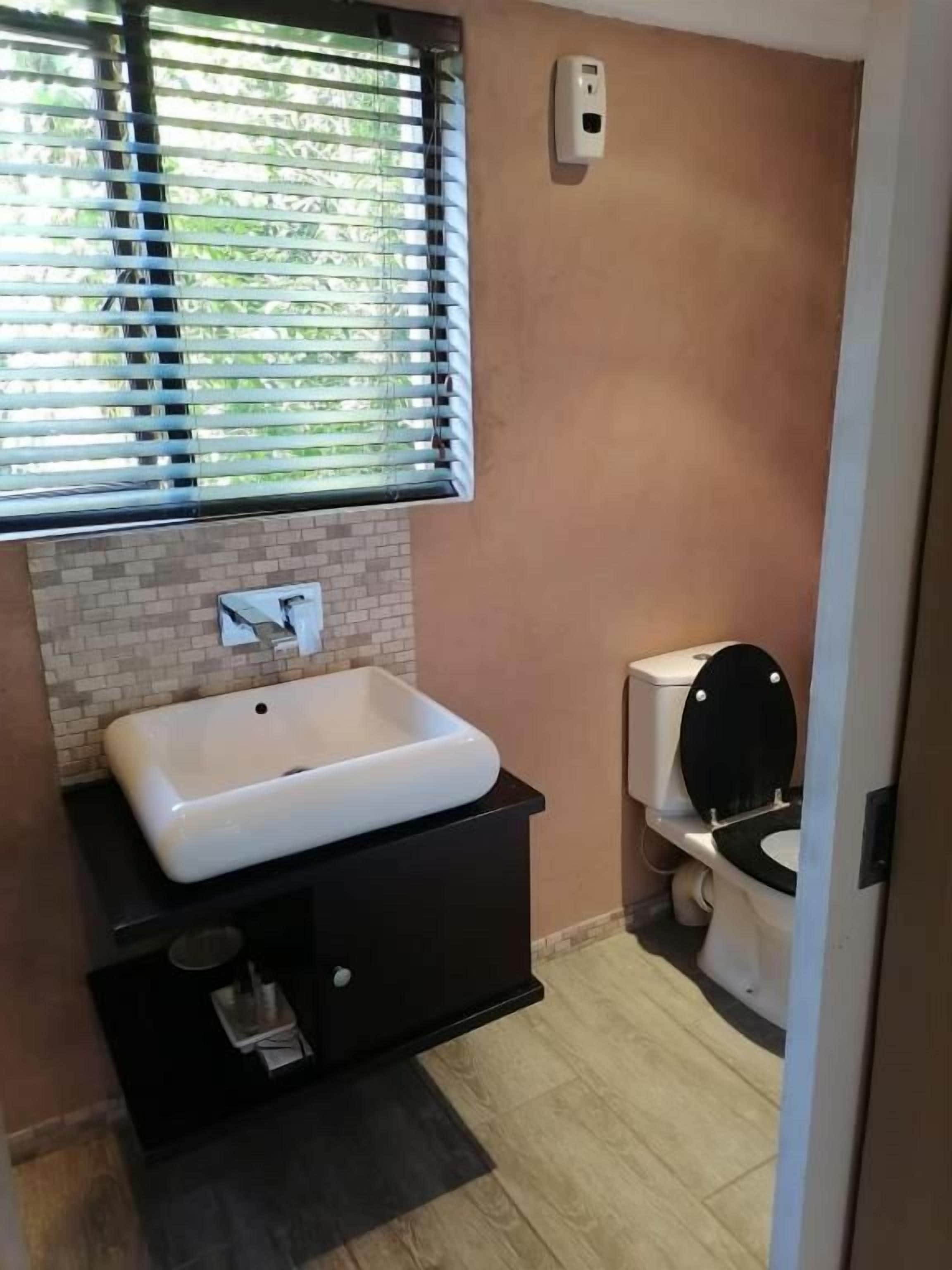 Un baño con lavamanos blanco, mueble negro y retrete.